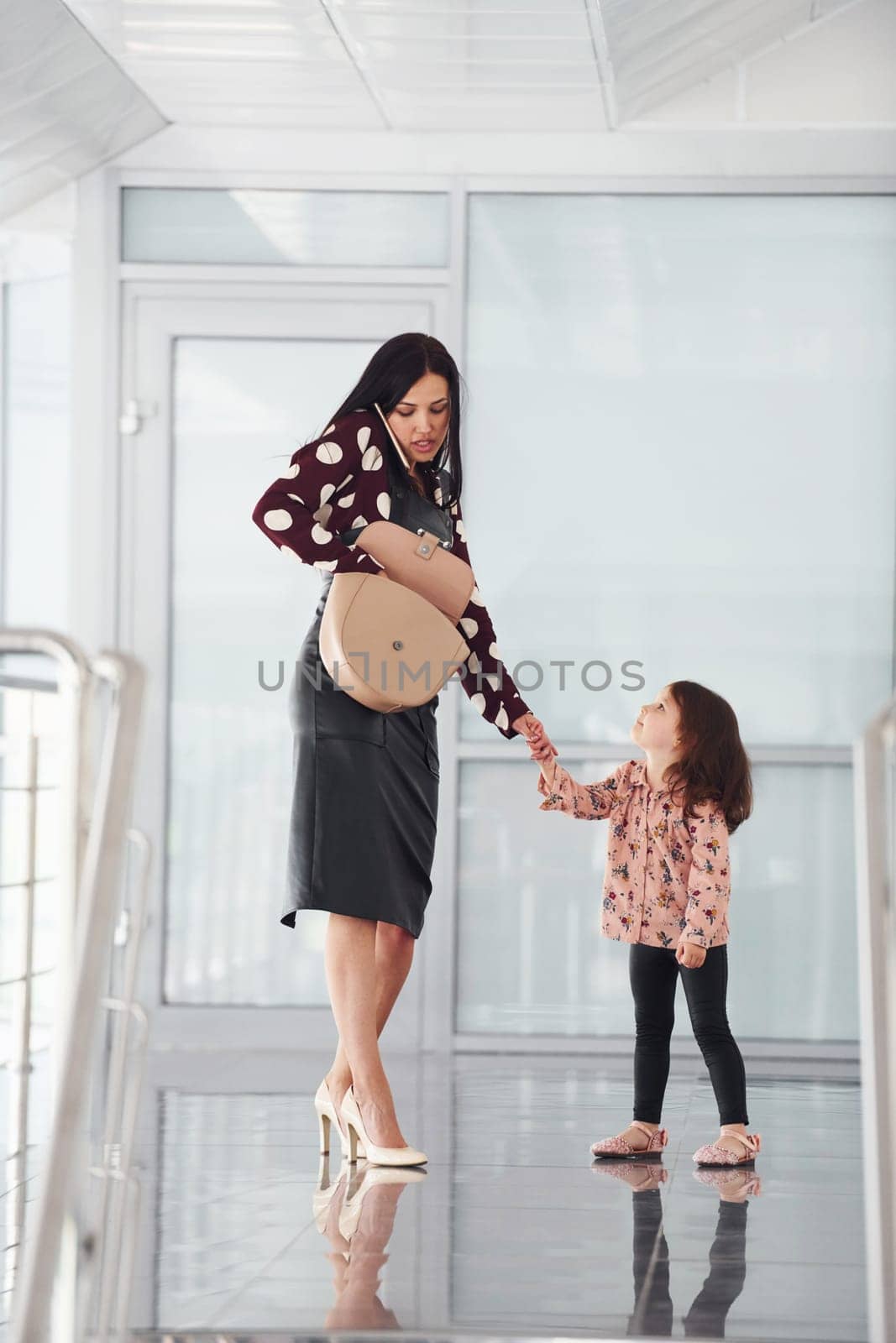 Young mother with her daughter walking together indoors in the office or airport. Having vacation.