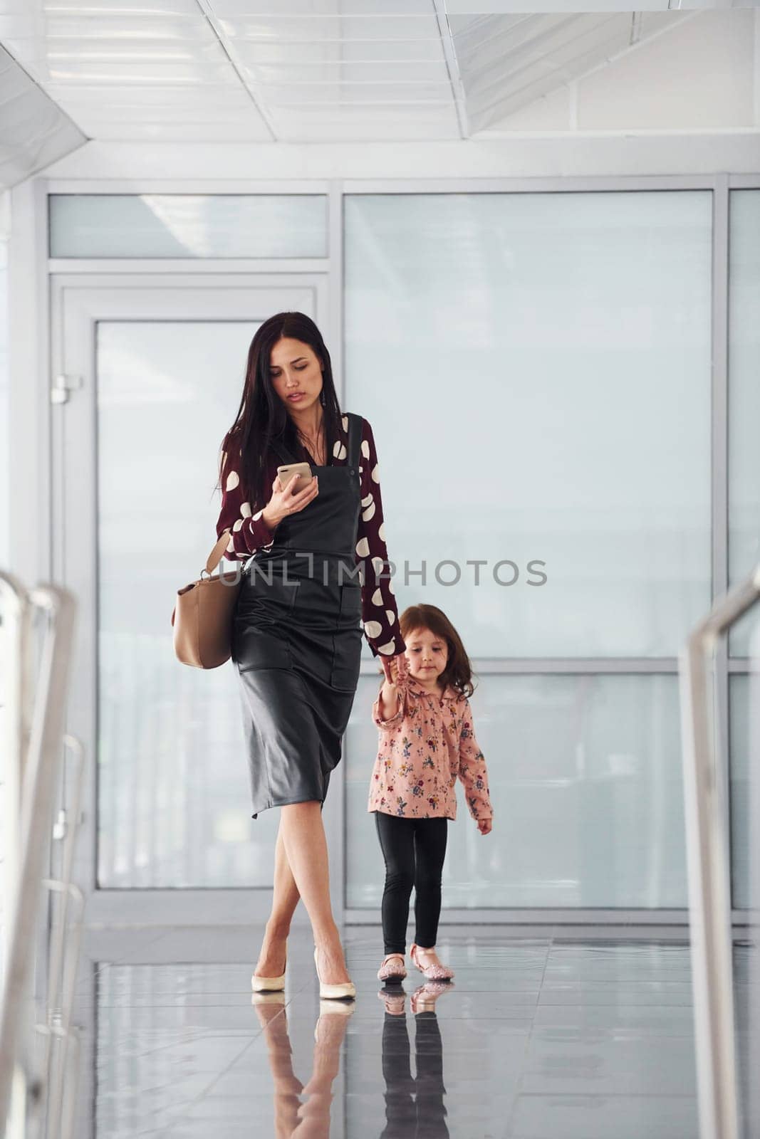 Young mother with her daughter walking together indoors in the office or airport. Having vacation.