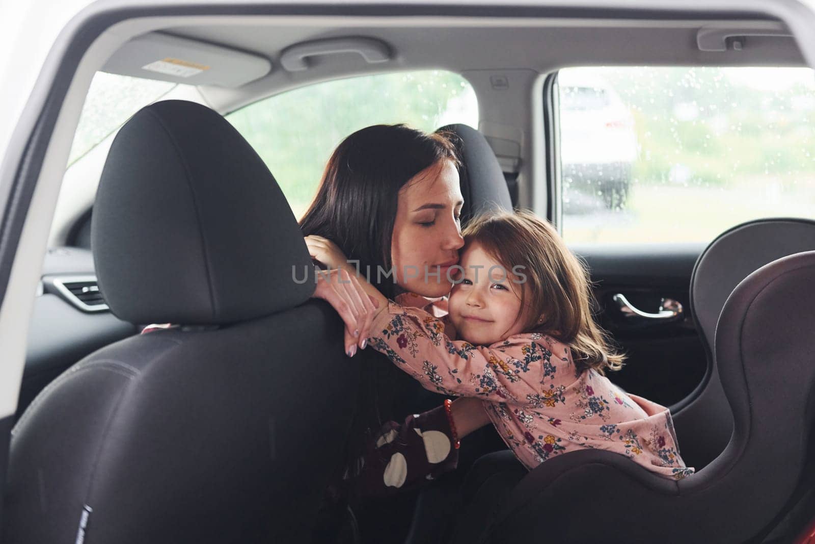 Embracing each other. Mother with her daughter inside of modern automobile together.