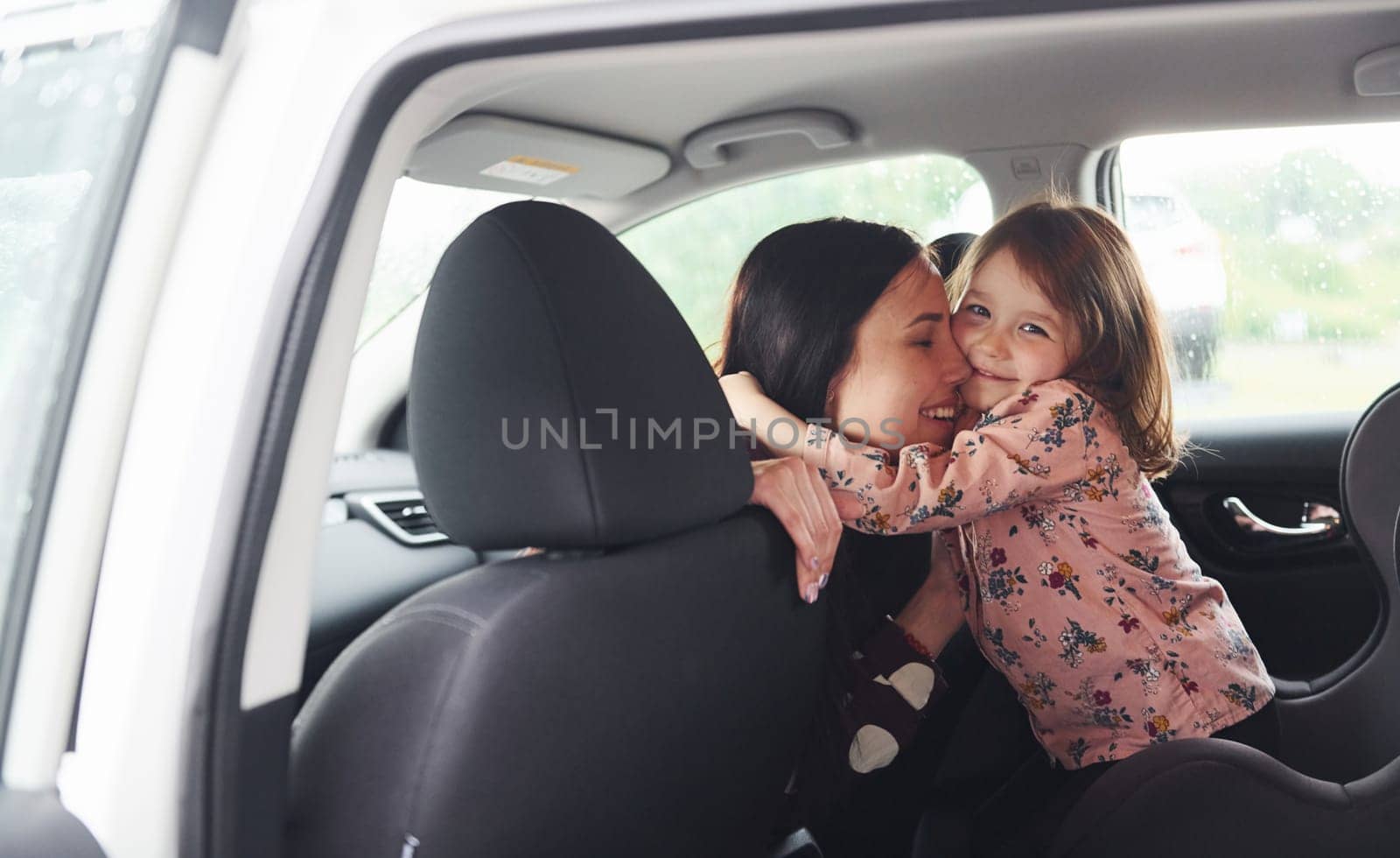 Embracing each other. Mother with her daughter inside of modern automobile together.