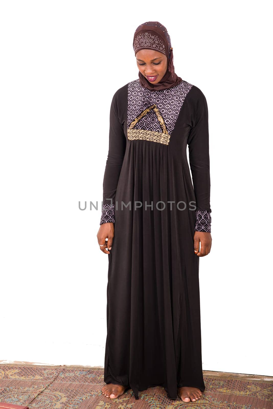young muslim woman standing in long dress with her head bowed smiling.