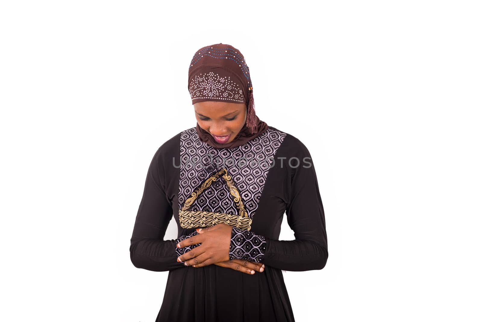 young muslim woman standing in long dress looking down hands crossed smiling.
