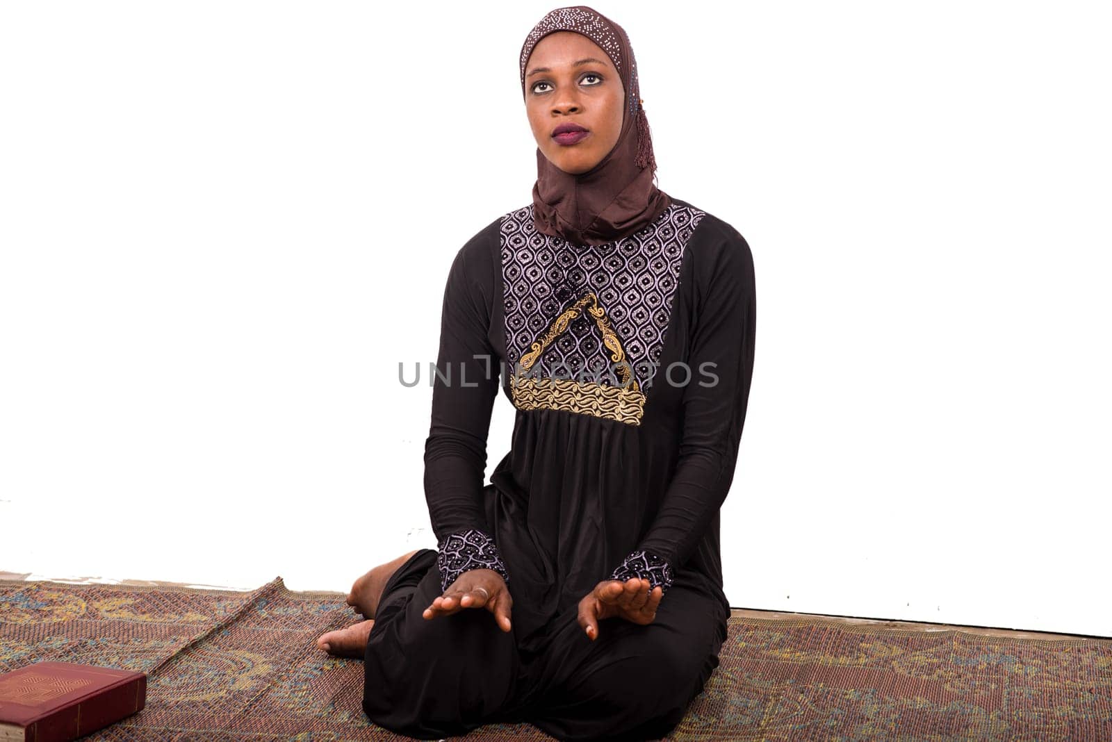 young muslim woman sitting in long dress on mat praying.