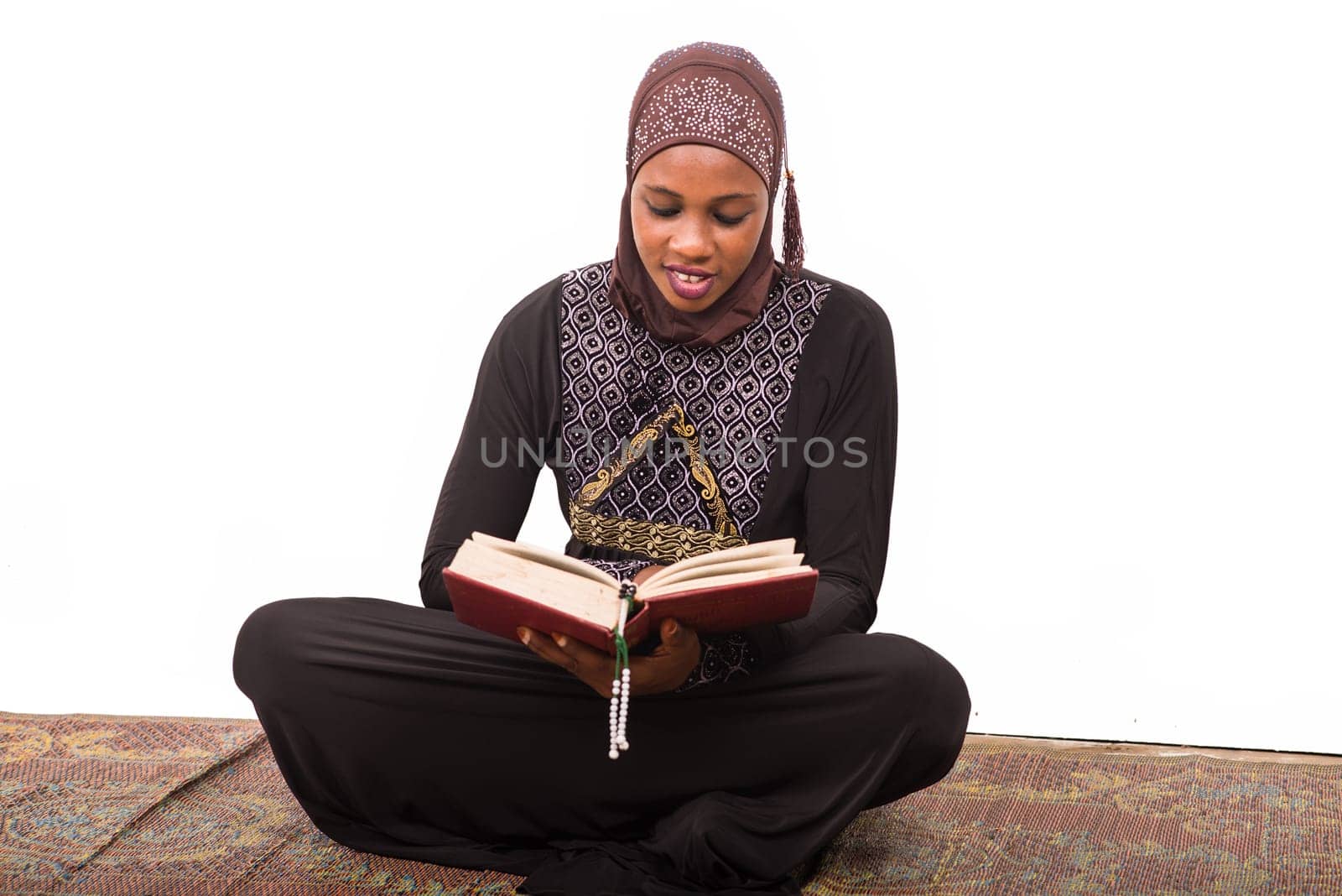 young muslim woman sitting on a mat reading the koran smiling.