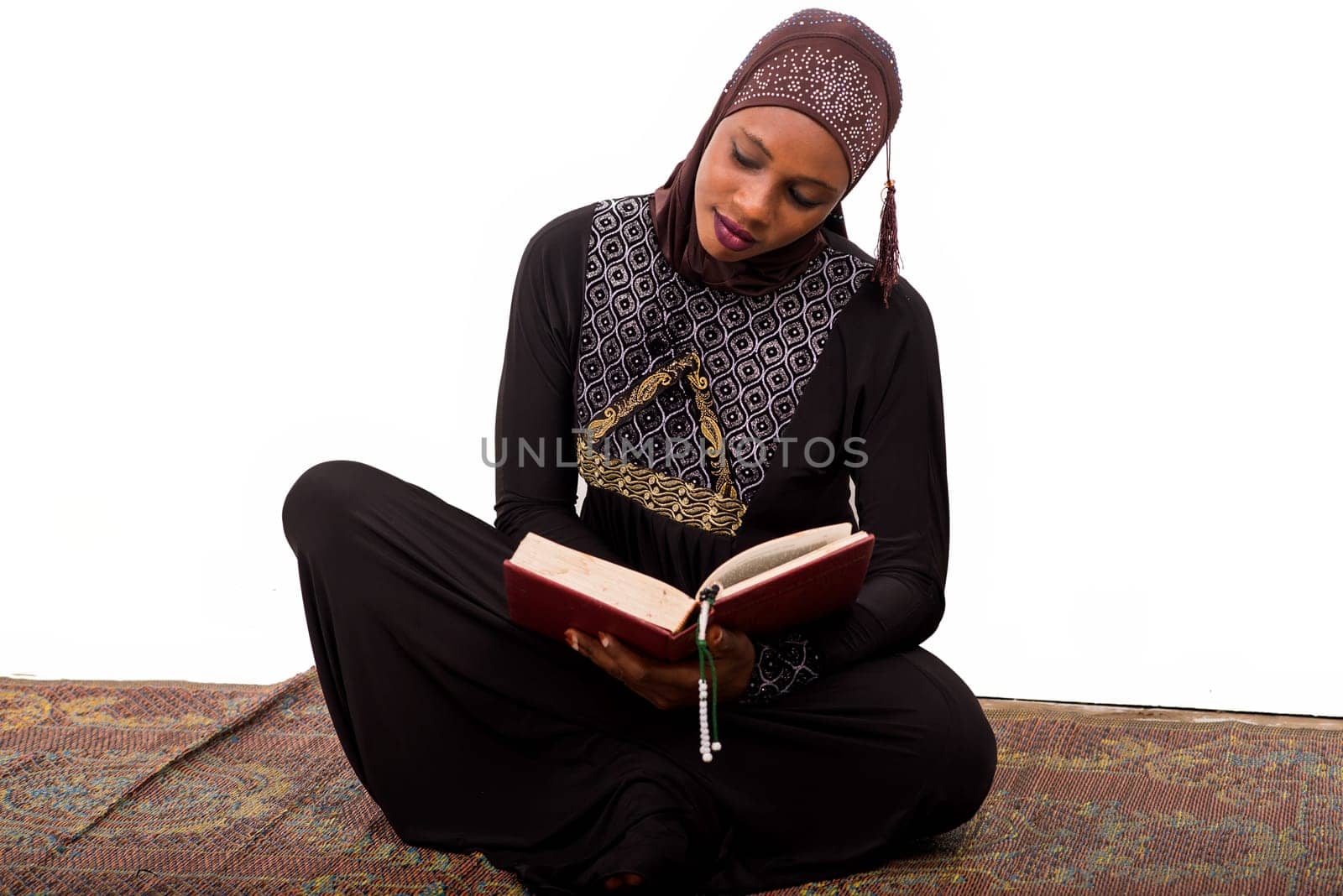 young muslim woman sitting on a mat reading the koran.