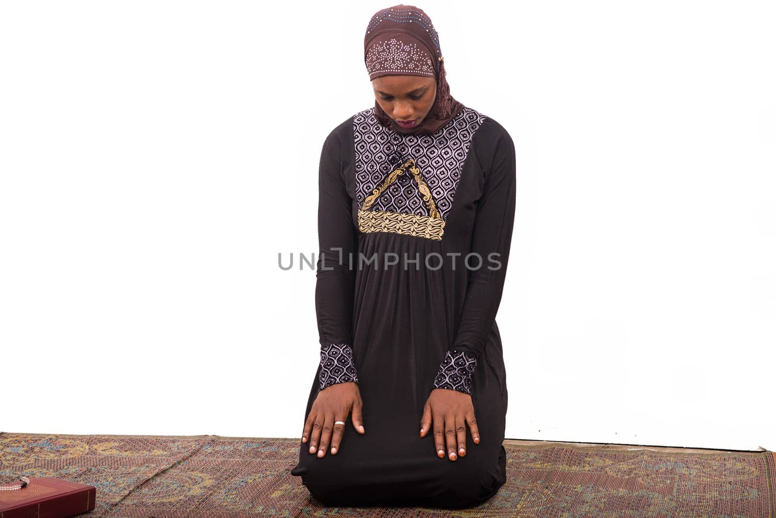 young muslim woman kneeling on a mat praying.