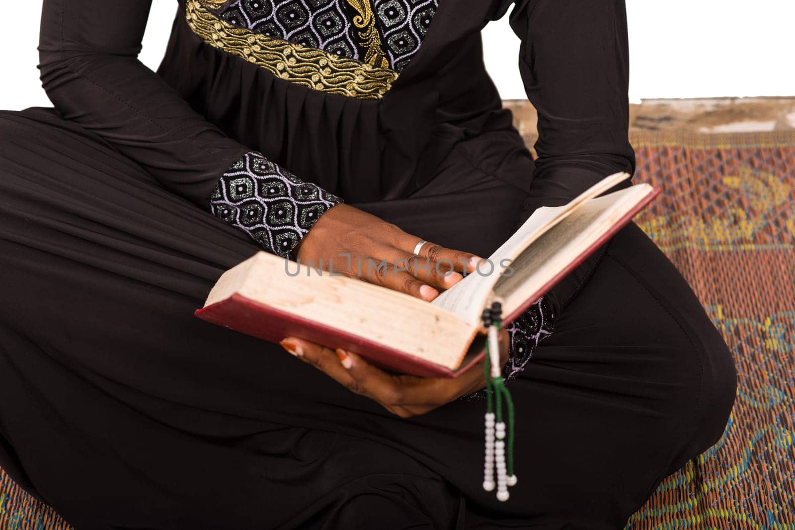 young muslim woman sitting on a mat reading the koran.