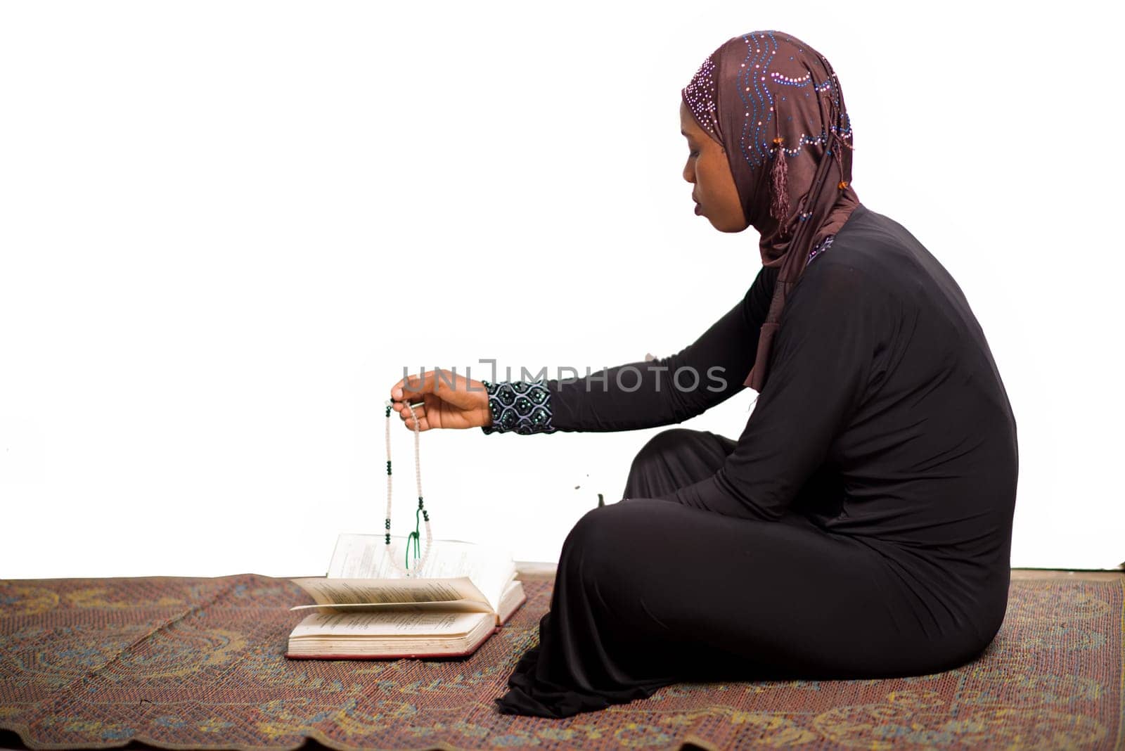 young muslim woman sitting on a mat praying rosary in hand.