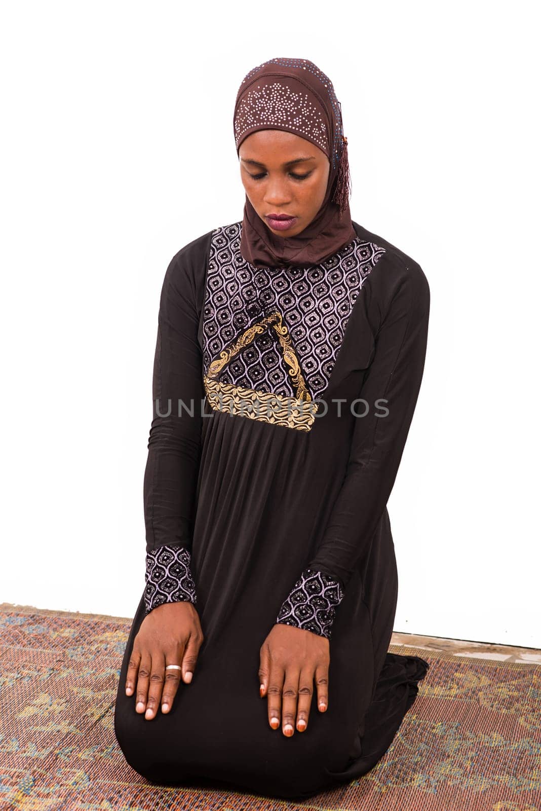 young muslim woman kneeling on mat praying.