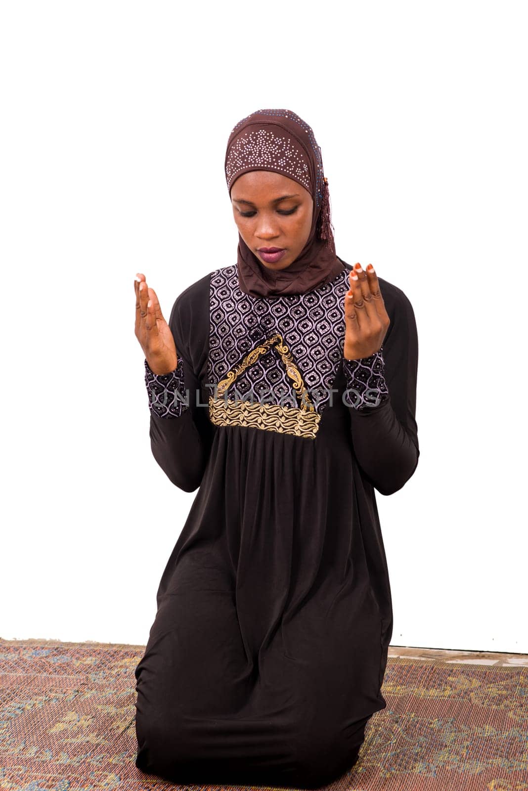 young muslim woman kneeling on mat praying.