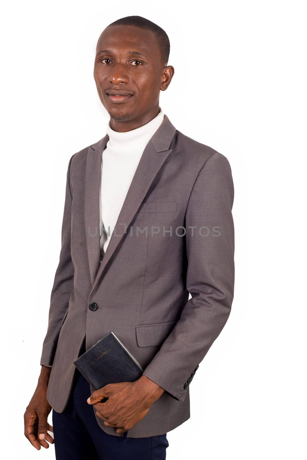young smiling pastor standing in jacket and holding a Bible on white background.