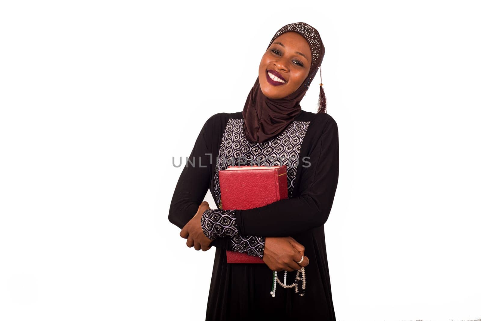 portrait of young smiling muslim woman standing holding a rosary and squeezing a red book against her chest