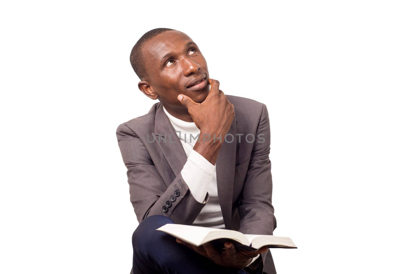 portrait of young pastor sitting cross-legged, hand under chin and looking up with a bible in the other hand.