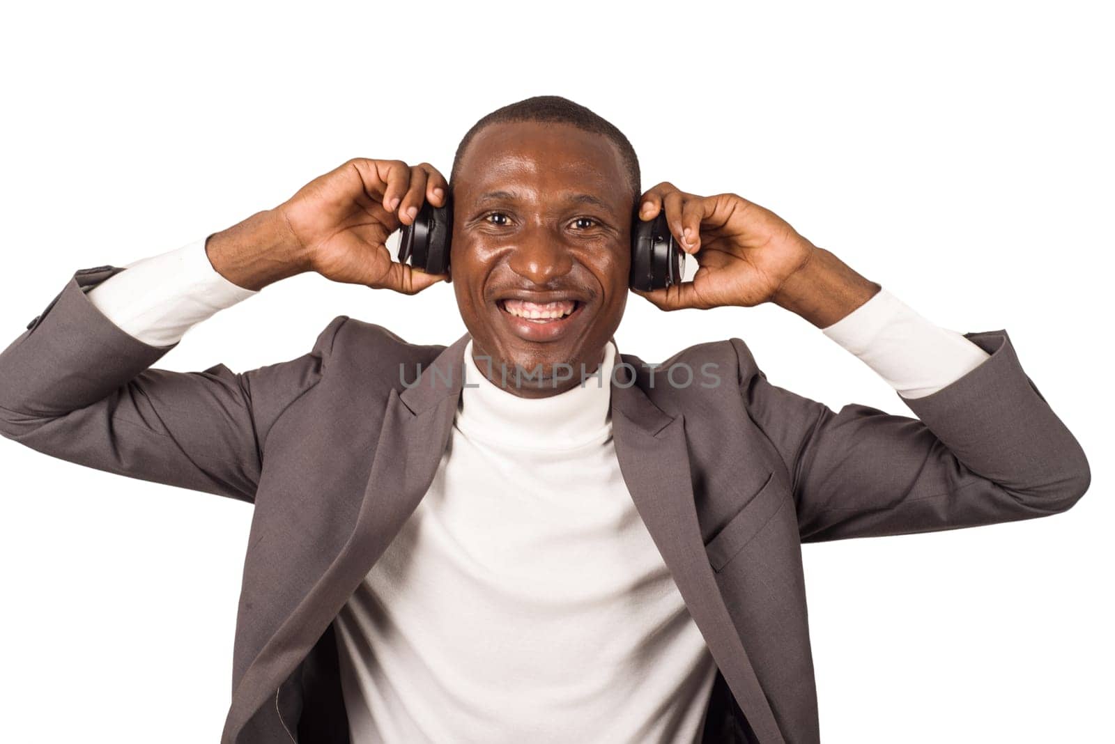 portrait of young man in suit standing and listening to music with headphones while smiling isolated on white background.