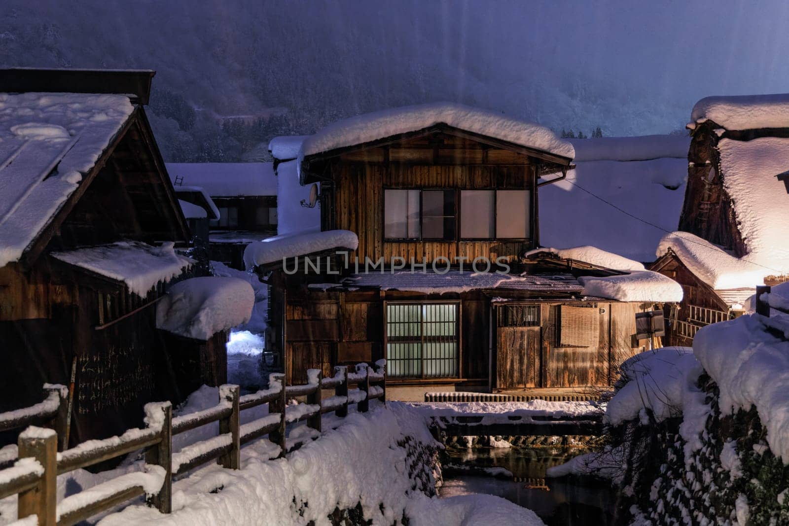 Heavy snow falls on traditional wooden homes in Japanese village at night. High quality photo