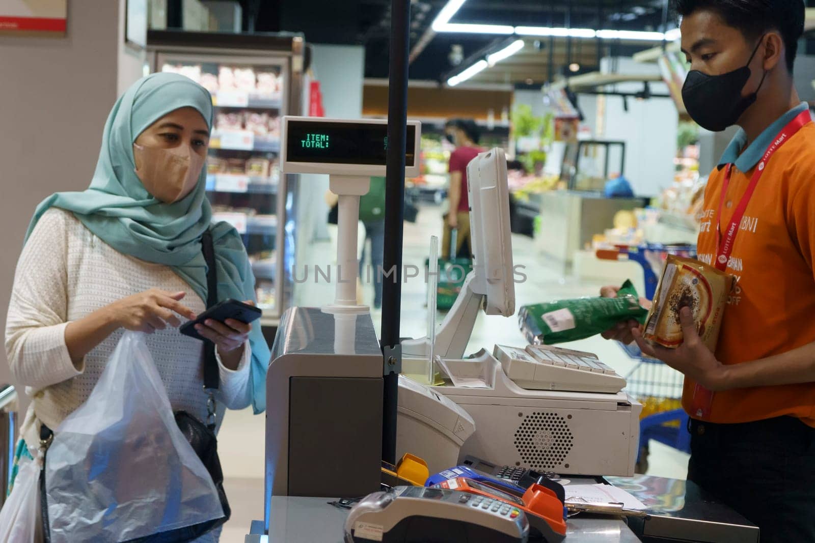 March 25, 2023. Muslim woman paying her shopping with her smartphone in grocery store in Surabaya, Indonesia in Ramadhan 2023.
