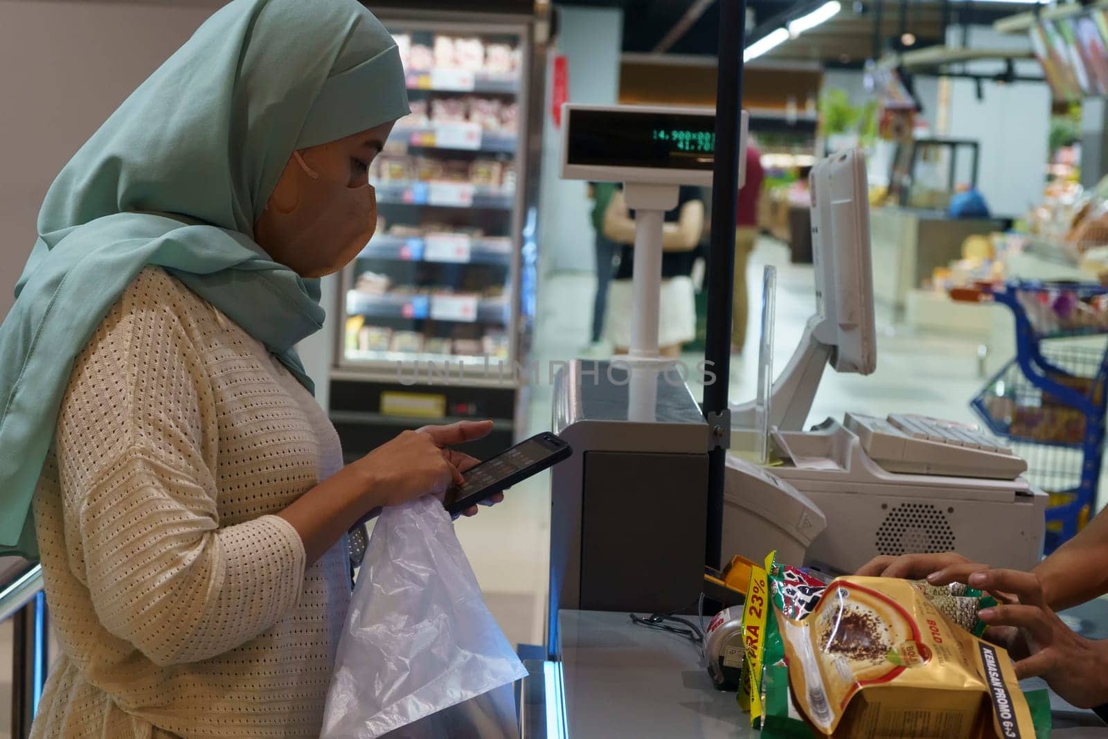 March 25, 2023. Muslim woman paying her shopping with her smartphone in grocery store in Surabaya, Indonesia in Ramadhan 2023.