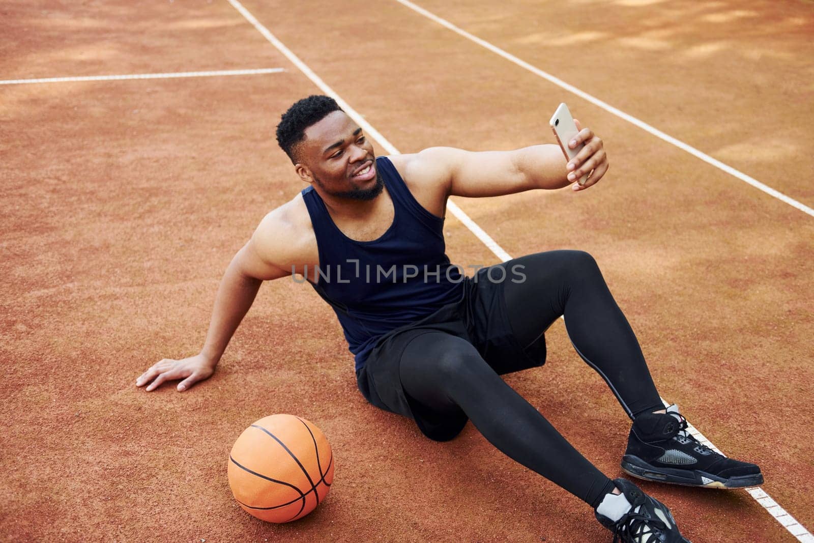 Making selfie. African american man plays basketball on the court outdoors.