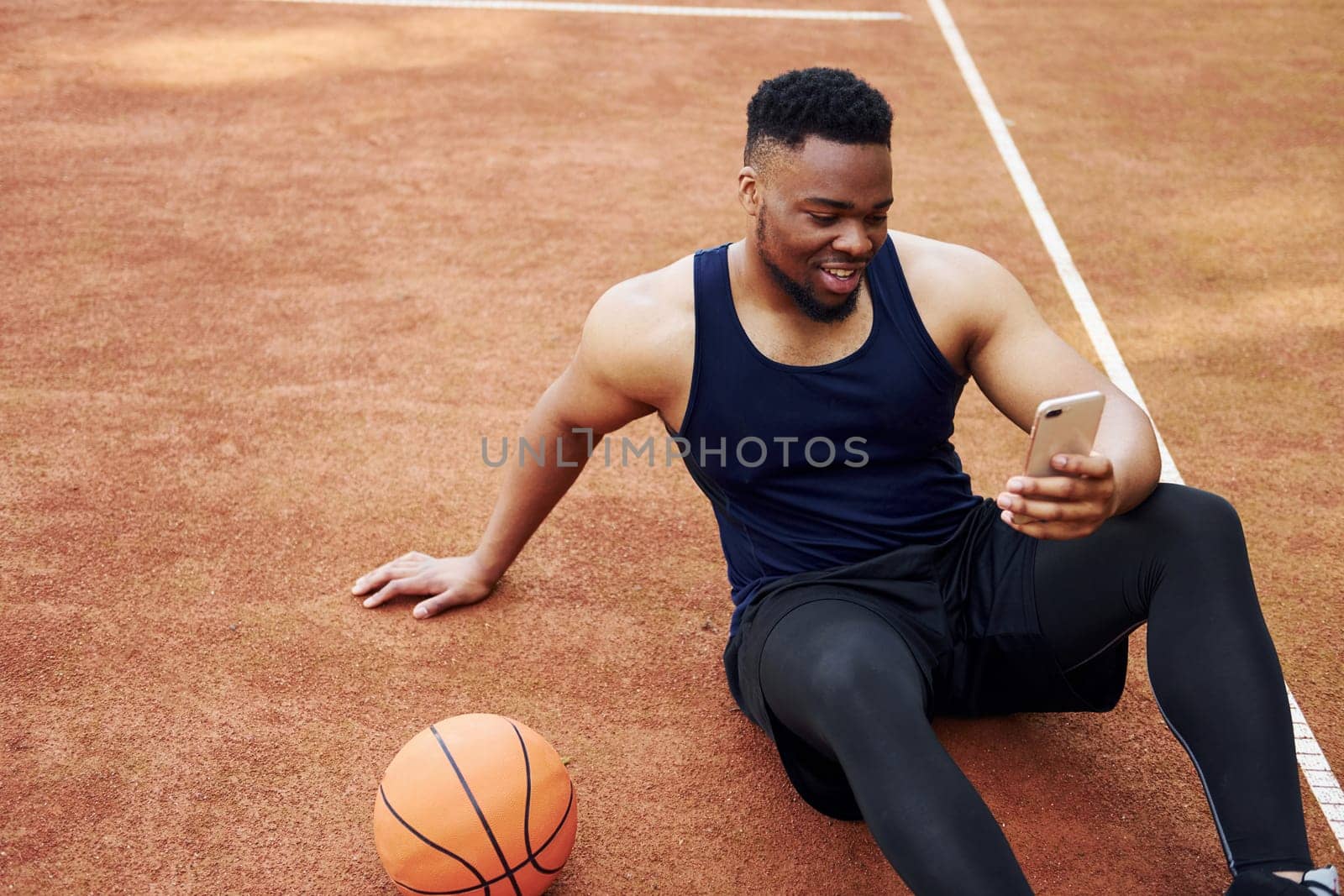 Using phone. African american man plays basketball on the court outdoors.