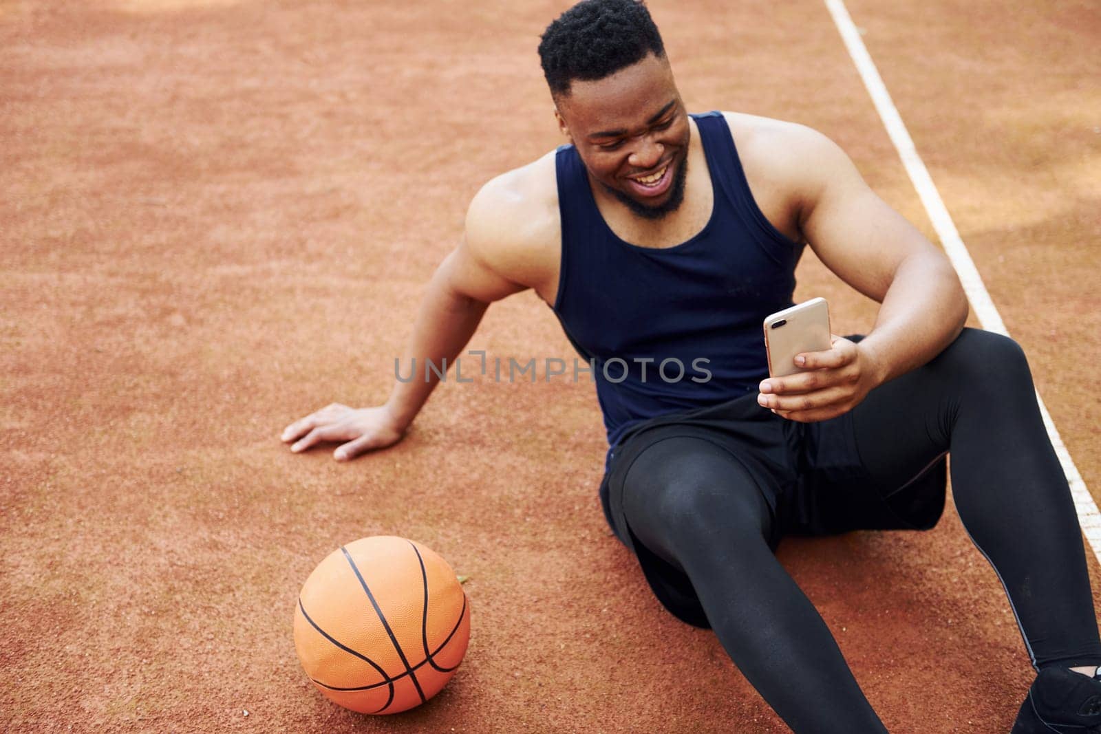 Using phone. African american man plays basketball on the court outdoors by Standret