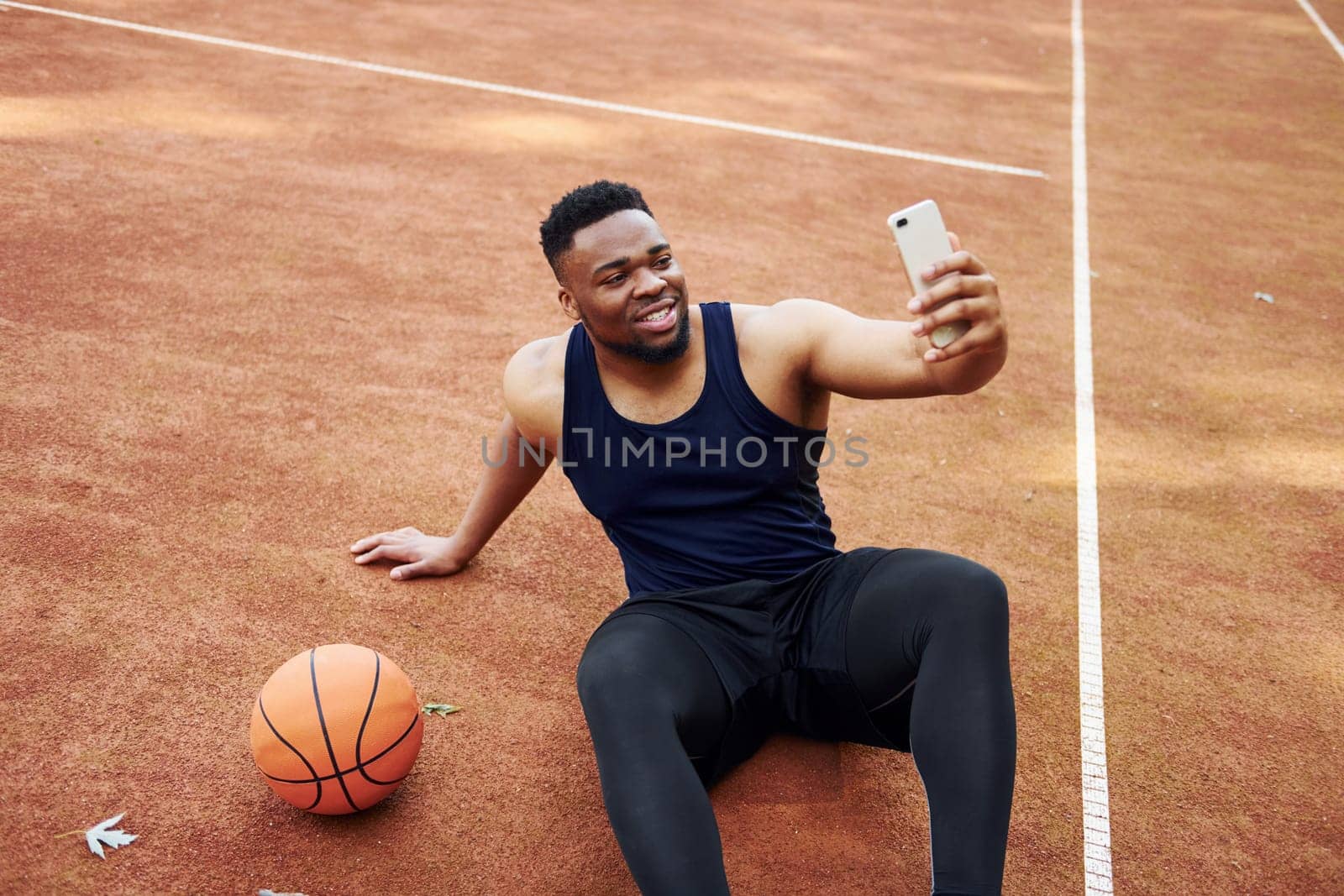 Making selfie. African american man plays basketball on the court outdoors.