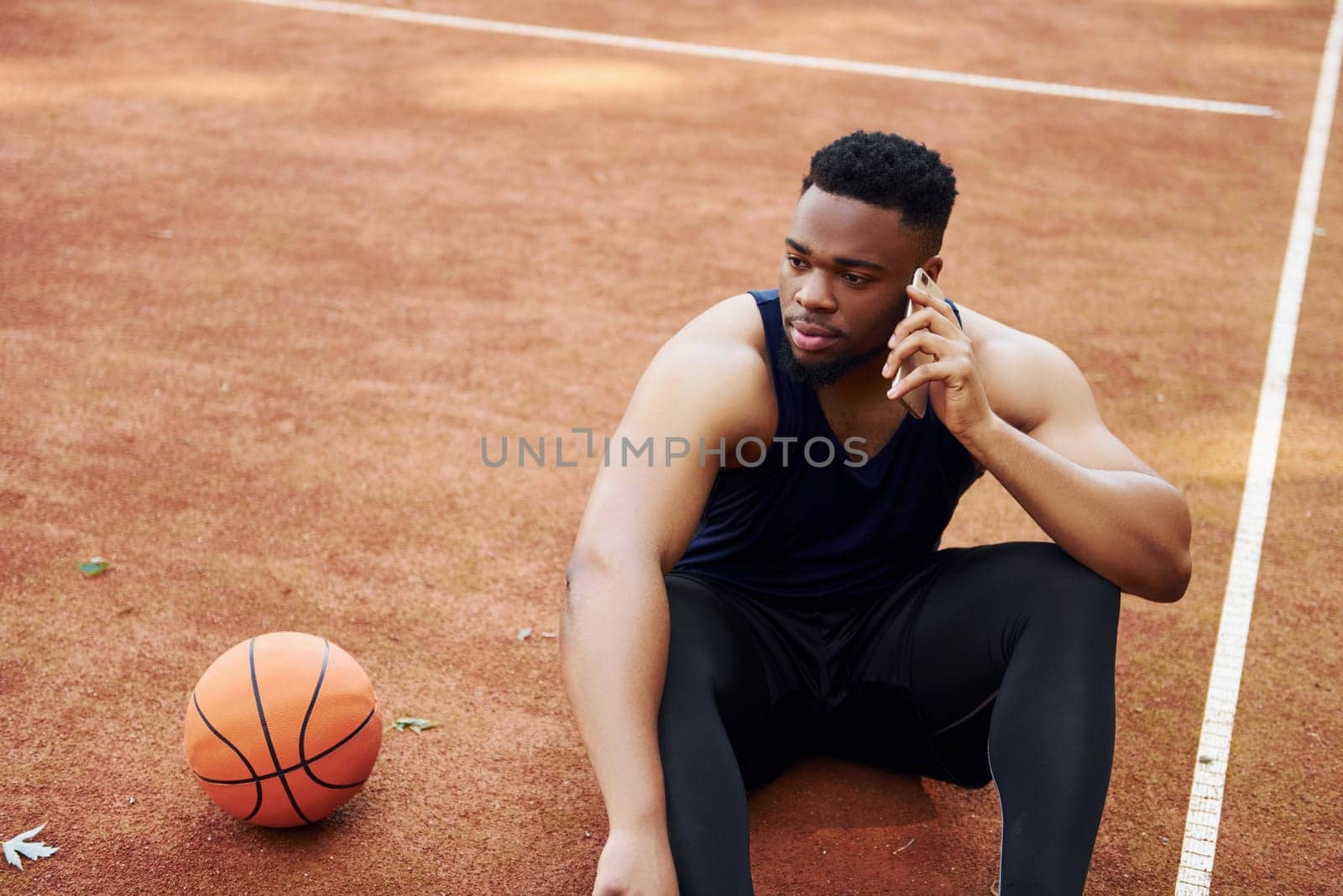 Talks by phone. African american man plays basketball on the court outdoors.