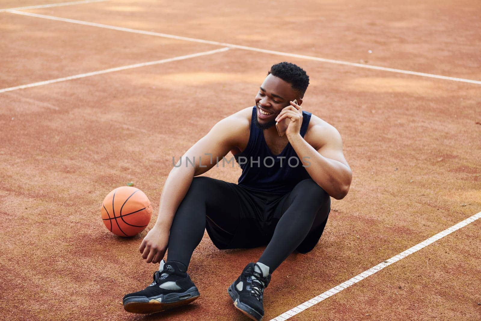 Talks by phone. African american man plays basketball on the court outdoors by Standret