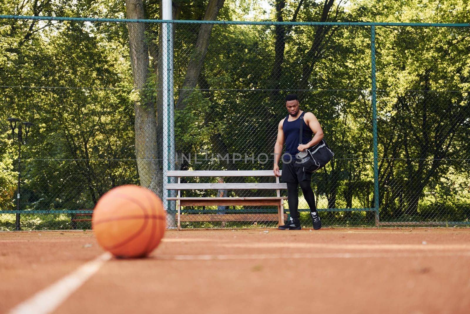 Beautiful green trees on background. African american man plays basketball on the court outdoors by Standret