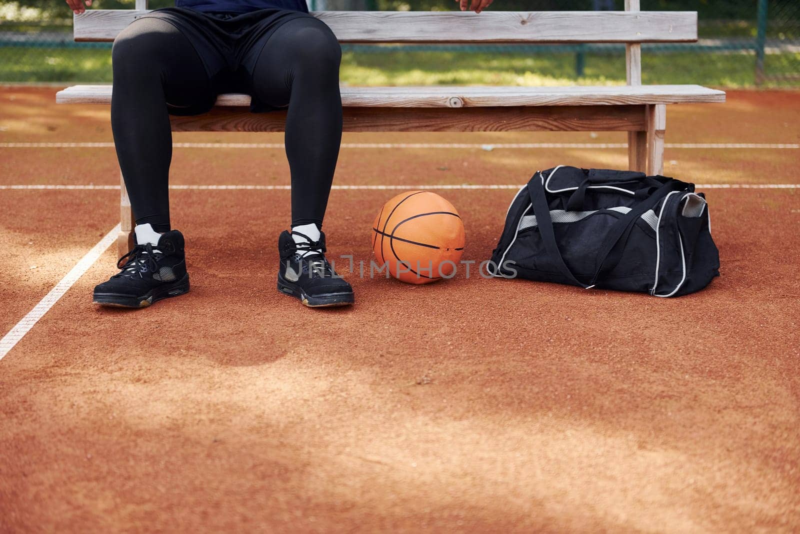 Sits with black bag and preparing for the game. African american man plays basketball on the court outdoors.
