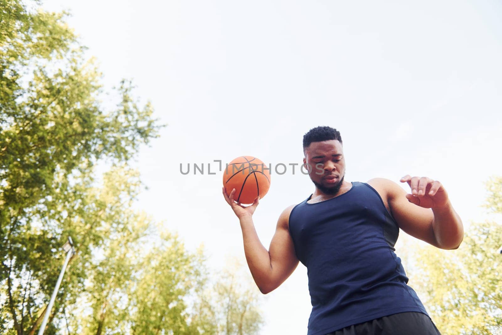 Cloudy weather. African american man plays basketball on the court outdoors by Standret