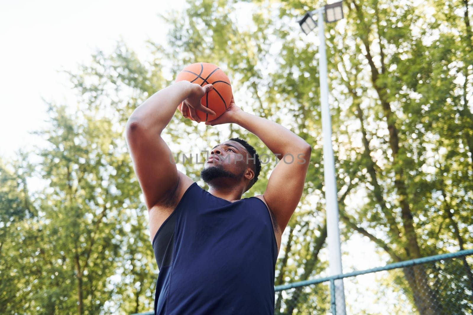 Cloudy weather. African american man plays basketball on the court outdoors by Standret