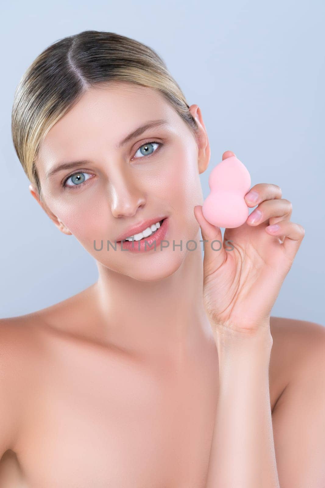 Alluring beautiful female model applying powder puff for facial makeup concept. Portrait of flawless perfect cosmetic skin woman put powder foundation on her face in isolated background.