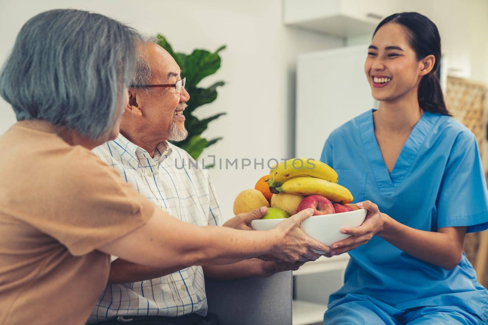 Contented senior couple taking a bowl of fruit from a nurse at home. by biancoblue