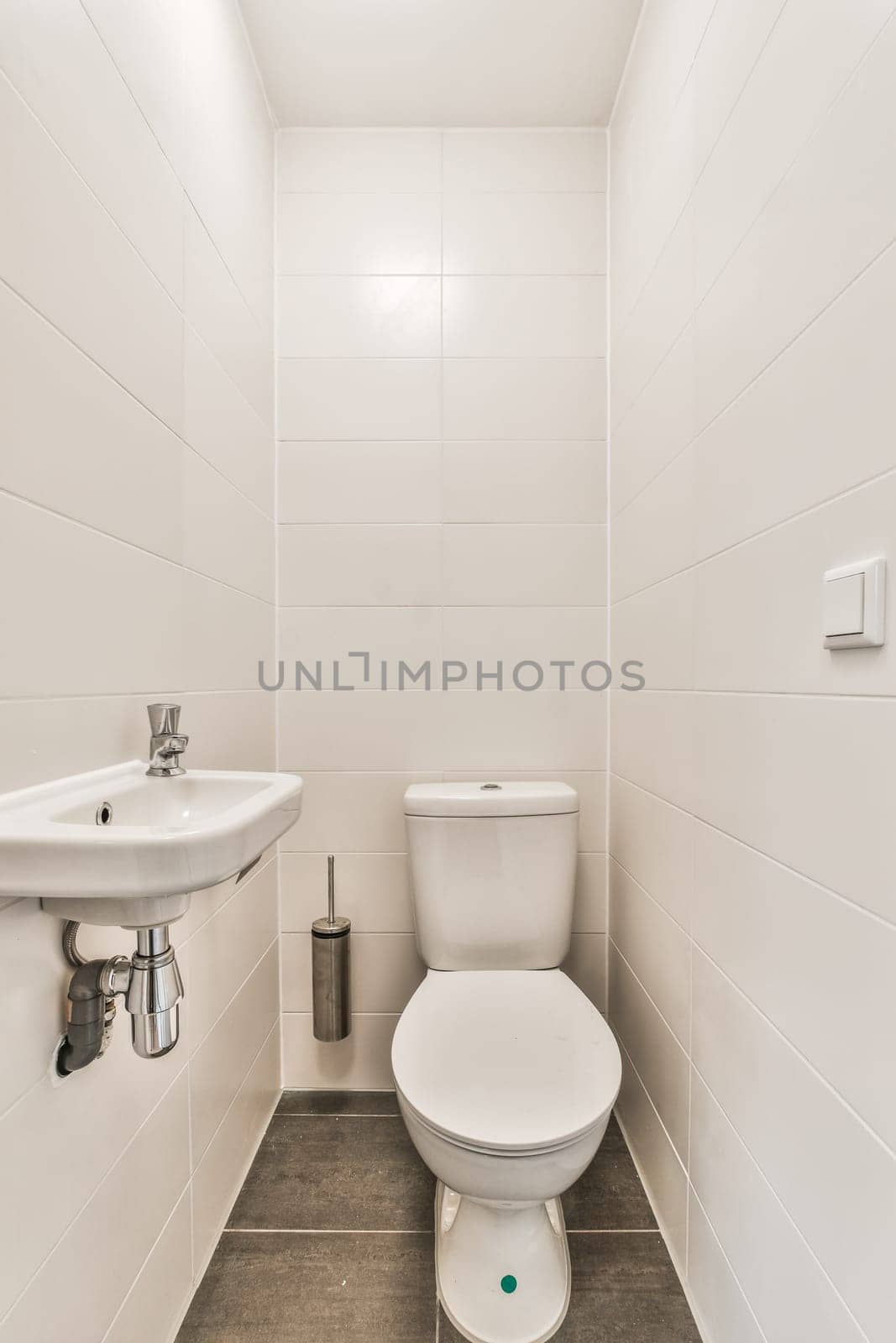 a bathroom with white tiles on the wall and toilet in the corner, there is a sink next to the toilet
