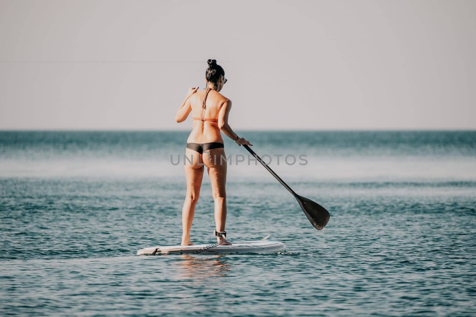 Sea woman sup. Silhouette of happy middle aged woman in rainbow bikini, surfing on SUP board, confident paddling through water surface. Idyllic sunset. Active lifestyle at sea or river