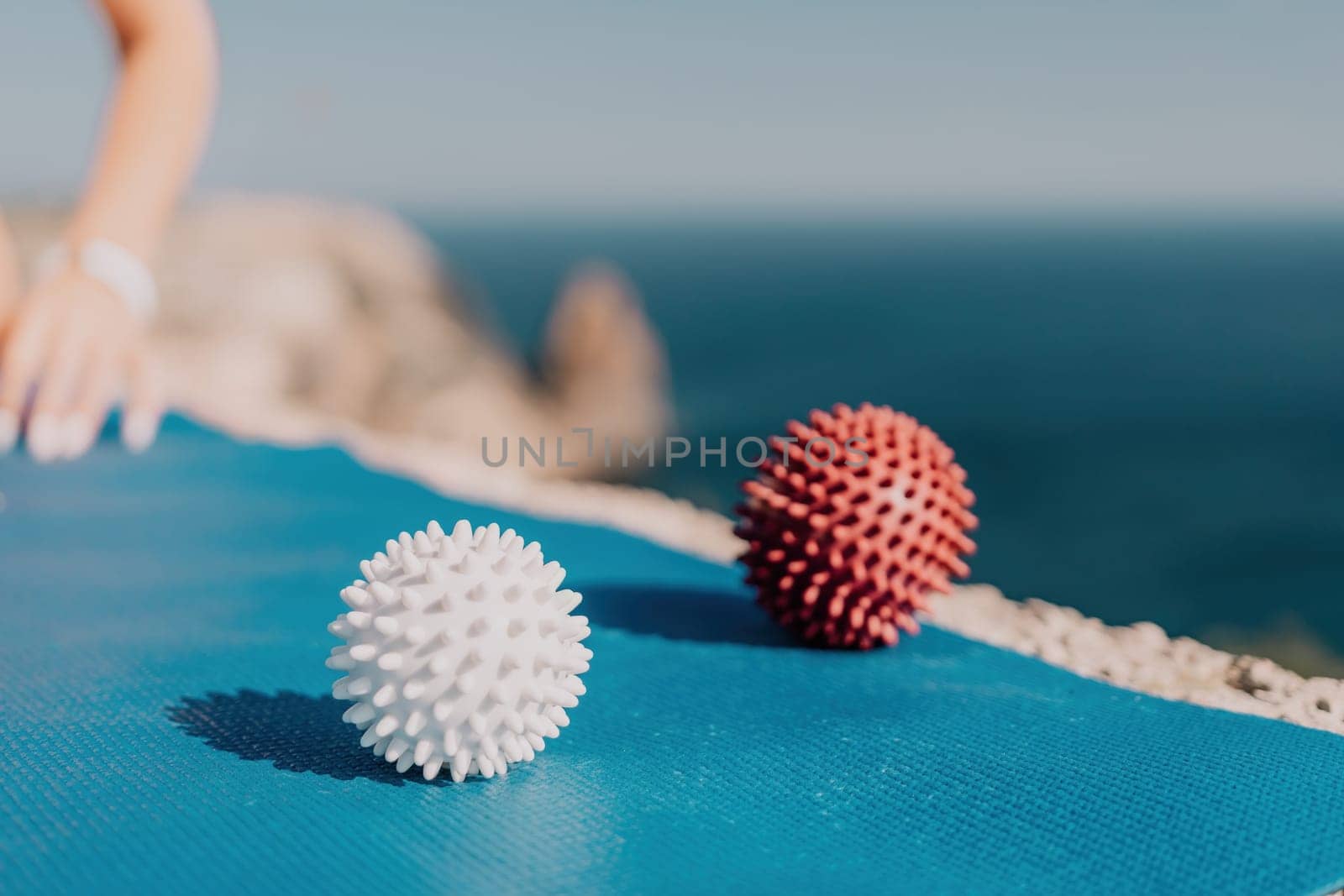 Woman sea pilates. Red and white massage balls are placed on a yoga mat, with the sea in the background. Healthy lifestyle, harmony and meditation. by panophotograph
