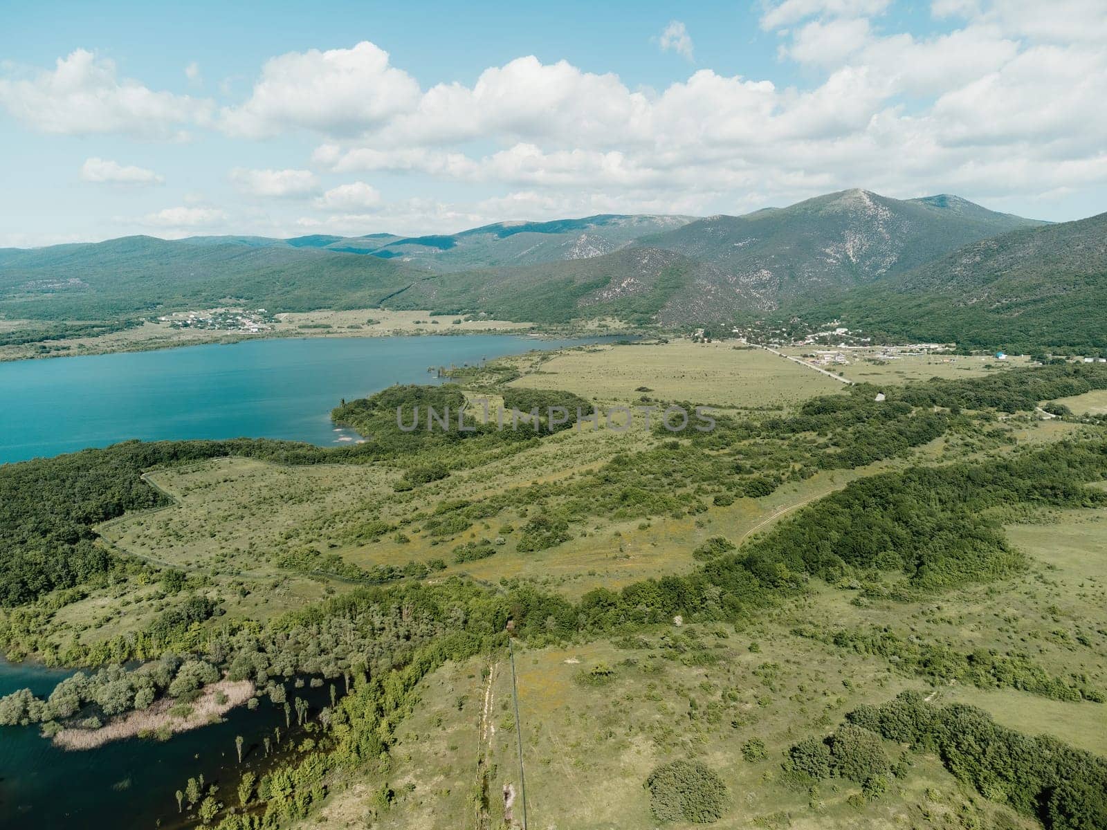 Aerial landscape from flying drone storage reservoir at mountain foot covered colorful spring forest. Beautiful view from above blue lake among highlands