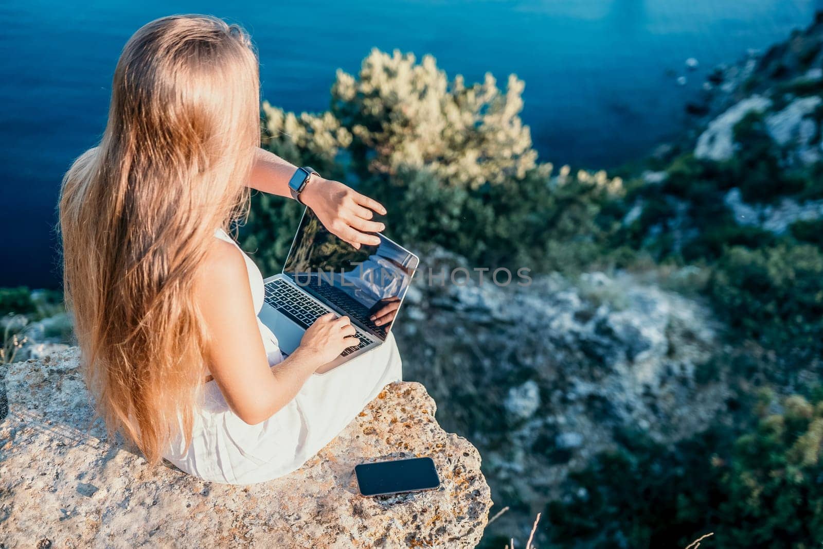 Digital nomad, Business woman working on laptop by the sea. Pretty lady typing on computer by the sea at sunset, makes a business transaction online from a distance. Freelance, remote work on vacation by panophotograph