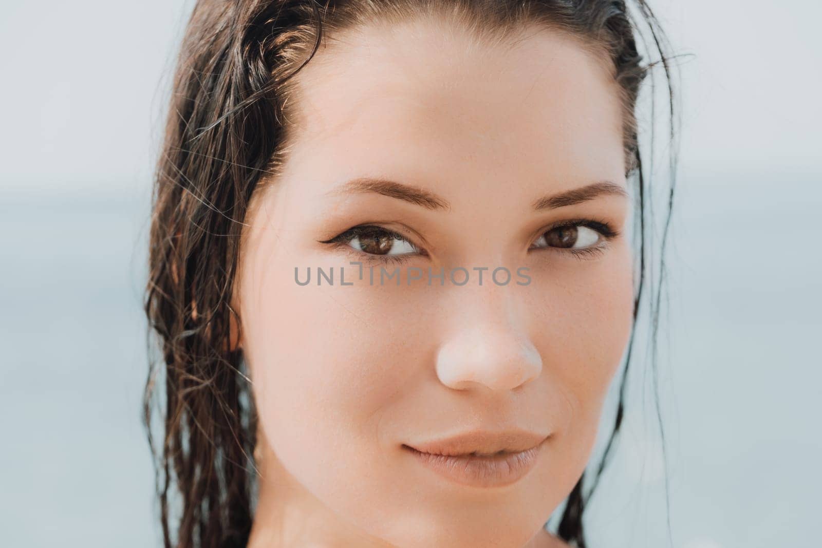 Close up shot of beautiful young caucasian woman with black hair and freckles looking at camera and smiling. Cute woman portrait in a pink bikini posing on a volcanic rock high above the sea