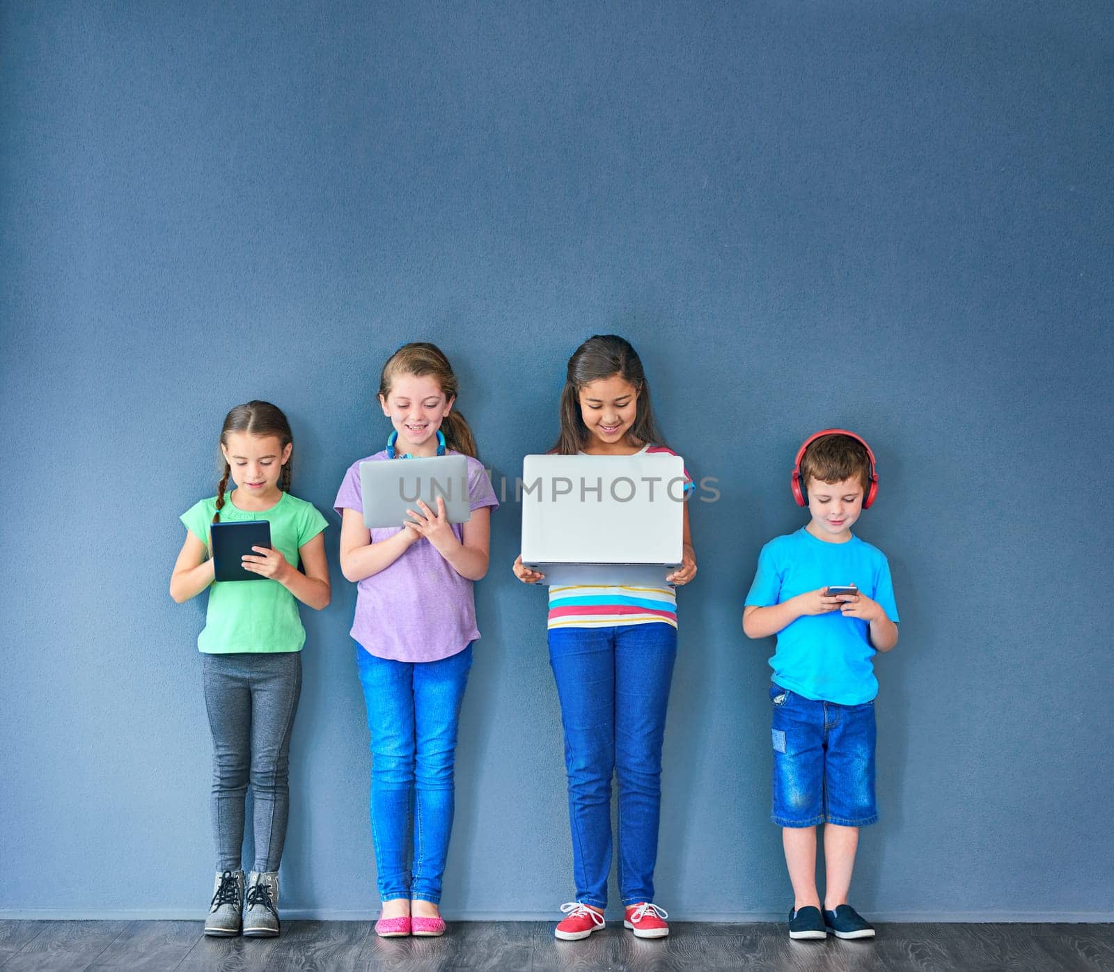 Leaving wireless technology in the hands of kids. Studio shot of a group of kids using wireless technology against a blue background. by YuriArcurs