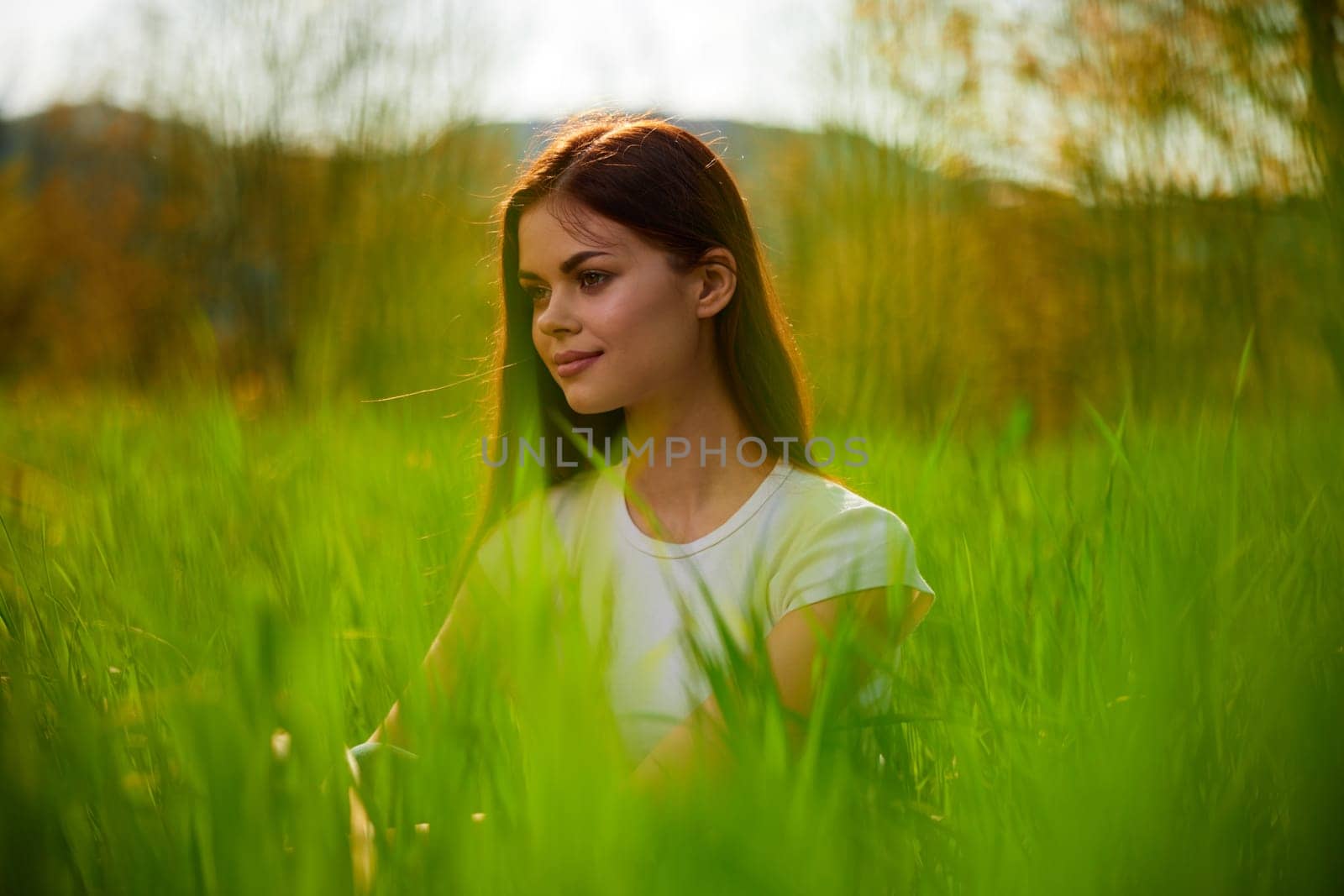 portrait of a happy woman in a white t-shirt shot through grass leaves in a field by Vichizh