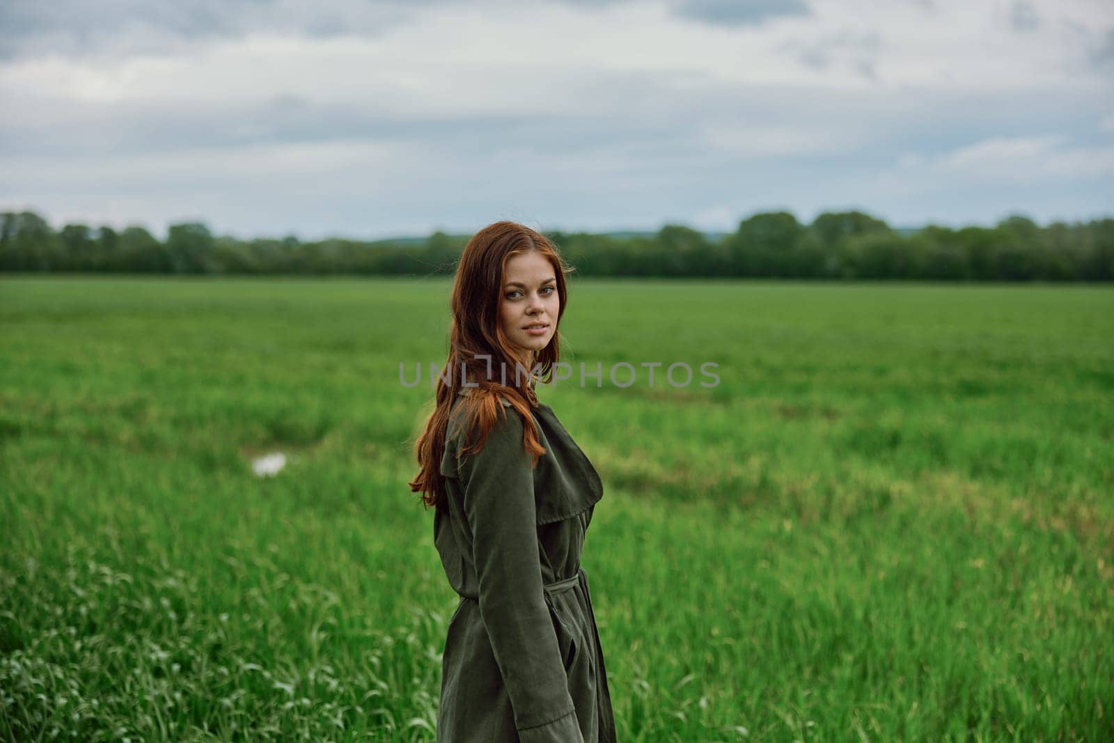 portrait of a beautiful, red-haired woman standing in a field in spring. Rainy weather, unity with nature. High quality photo