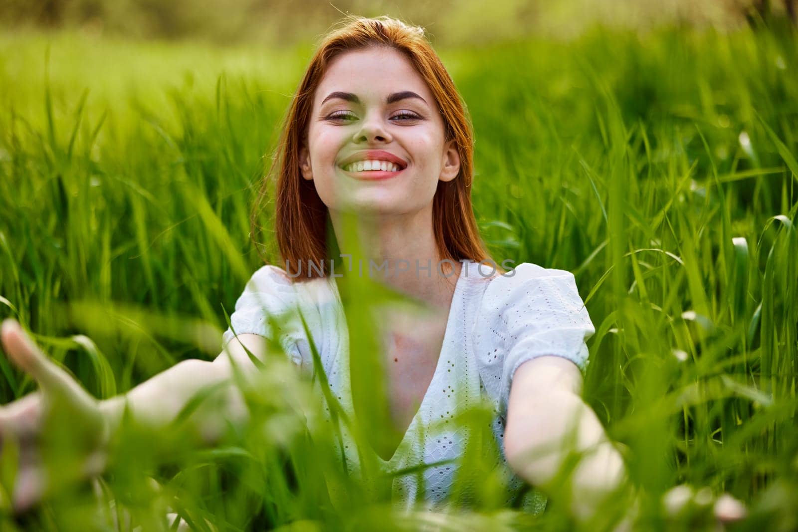 cheerful woman sitting in grass looking at camera smiling at camera by Vichizh