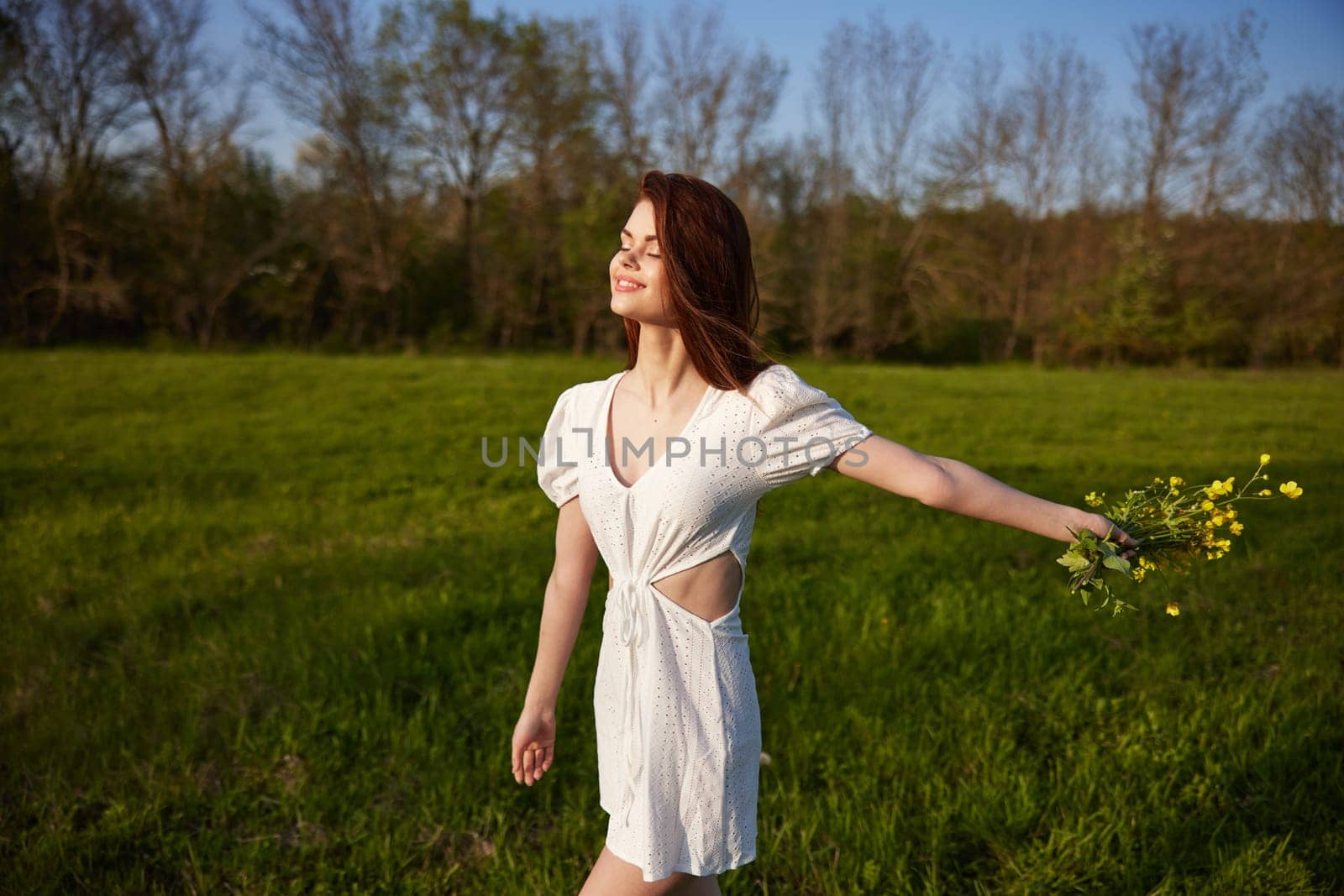 a beautiful, happy woman in a light dress stands in a field raising her hands high holding a bouquet of flowers. High quality photo