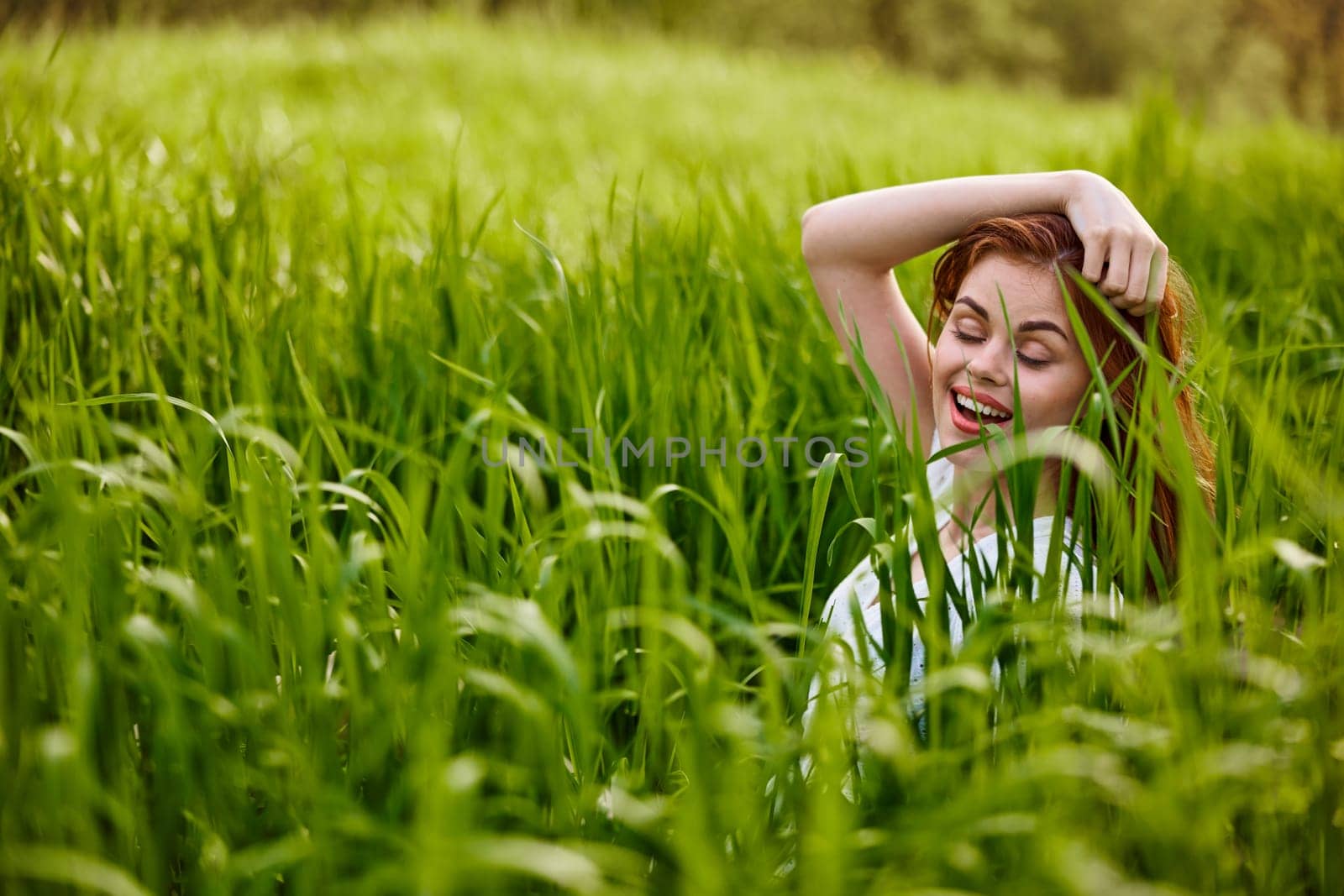 happy woman sitting in tall green grass holding her hair by Vichizh