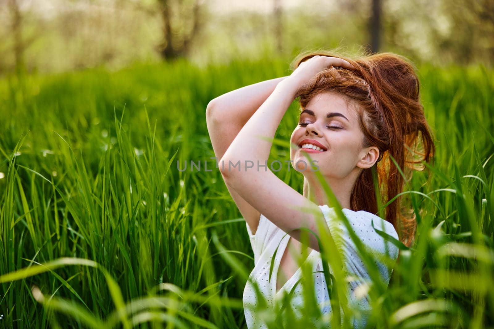 portrait of a beautiful woman sitting in tall grass and holding her long hair by Vichizh