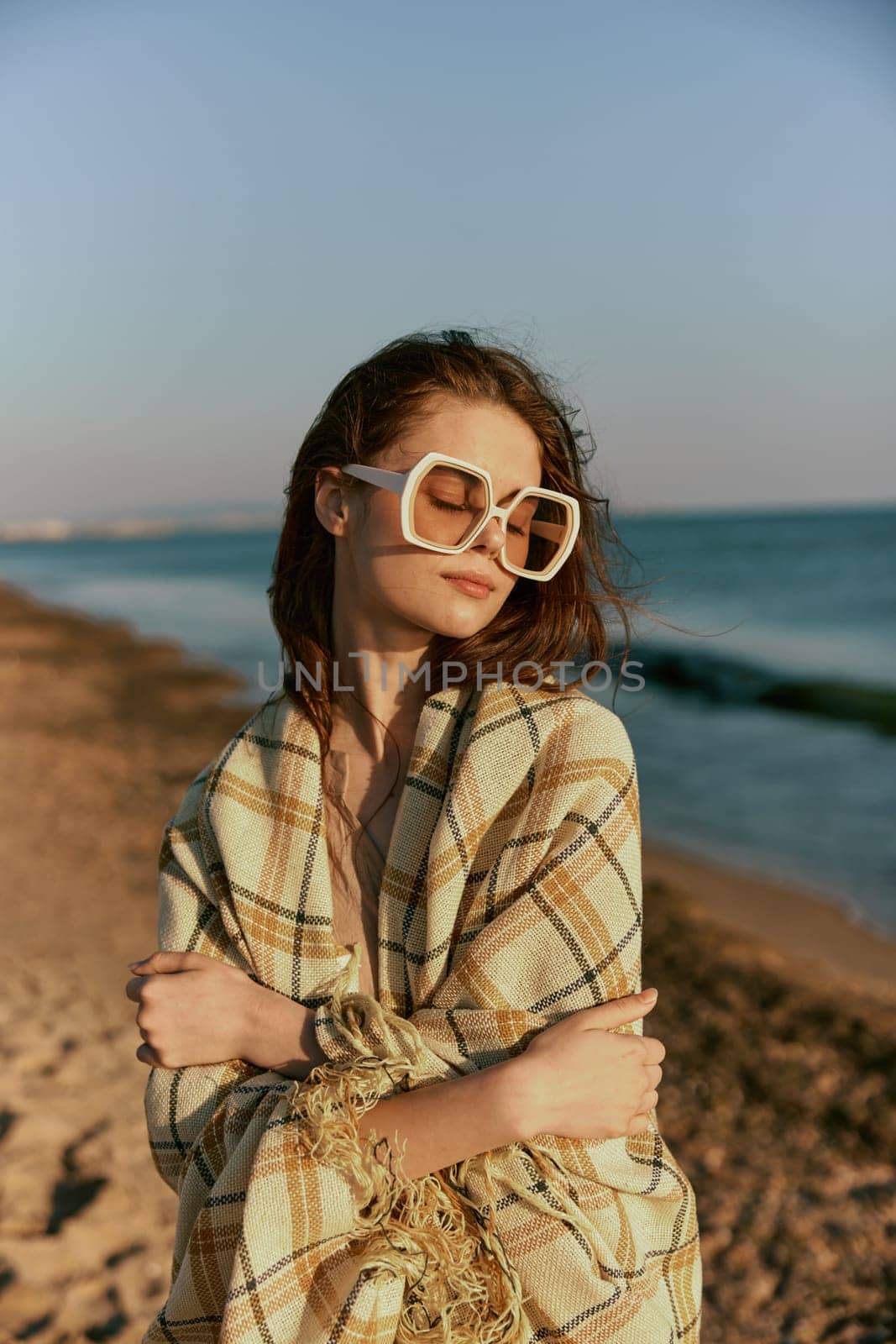 portrait of a woman in massive glasses wrapped in a plaid enjoying a warm day at the sea, facing the camera. High quality photo