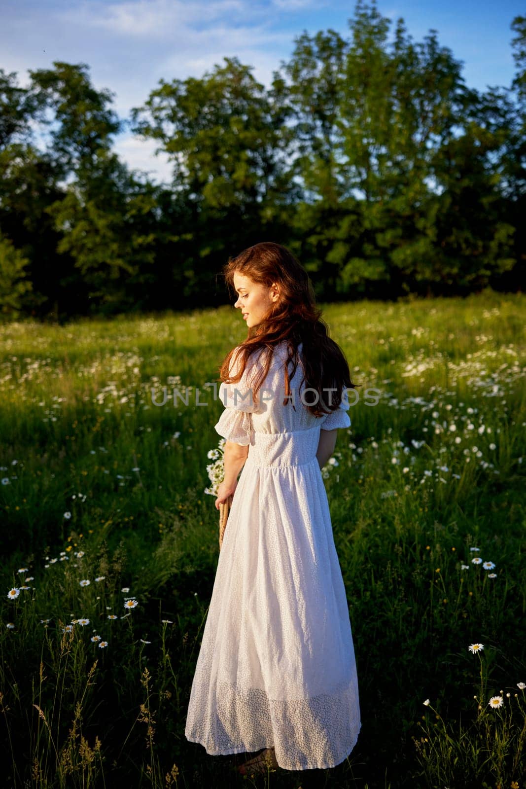a beautiful woman in a light, light, summer dress is standing in a flowering meadow in sunset lighting with her back to the camera by Vichizh