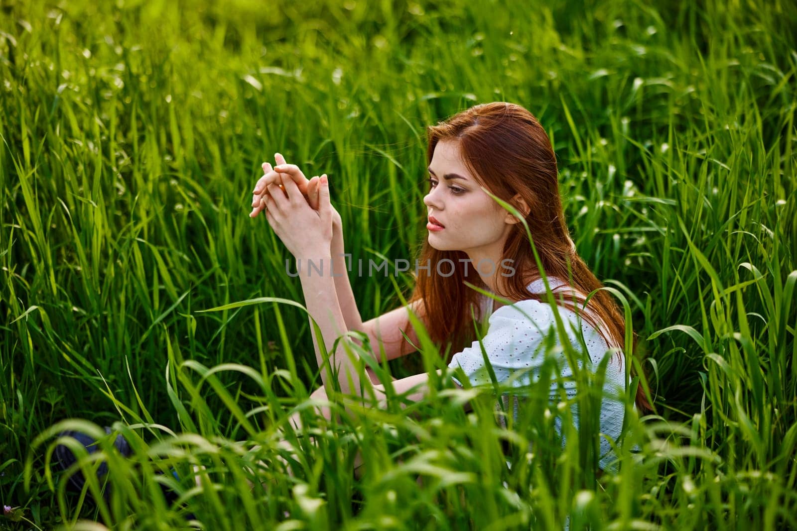 sad woman sitting in tall green grass on a sunny day. High quality photo