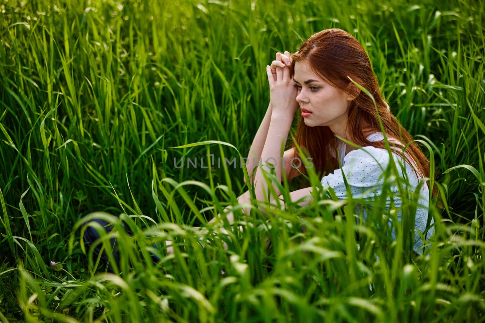 sad woman sitting in tall green grass on a sunny day by Vichizh